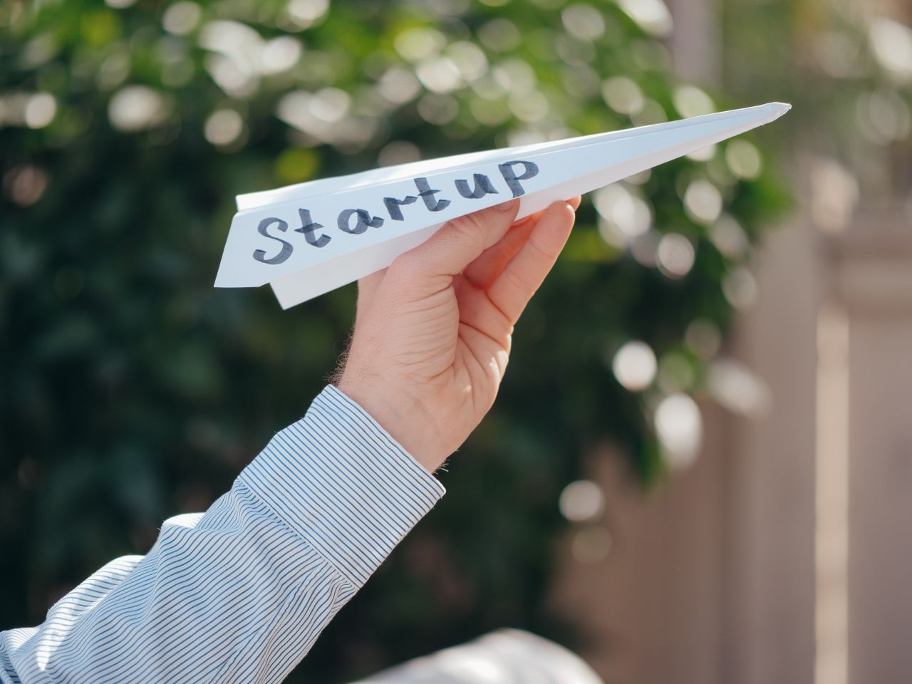 Close-up shot of a hand holding a paper airplane marked Startup, representing the launch of a business.
